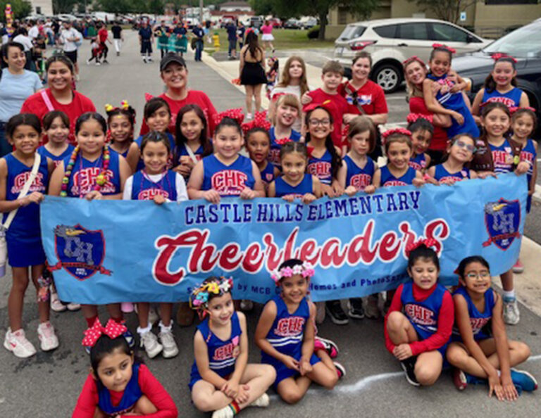 Young cheerleaders posing around a parade banner.